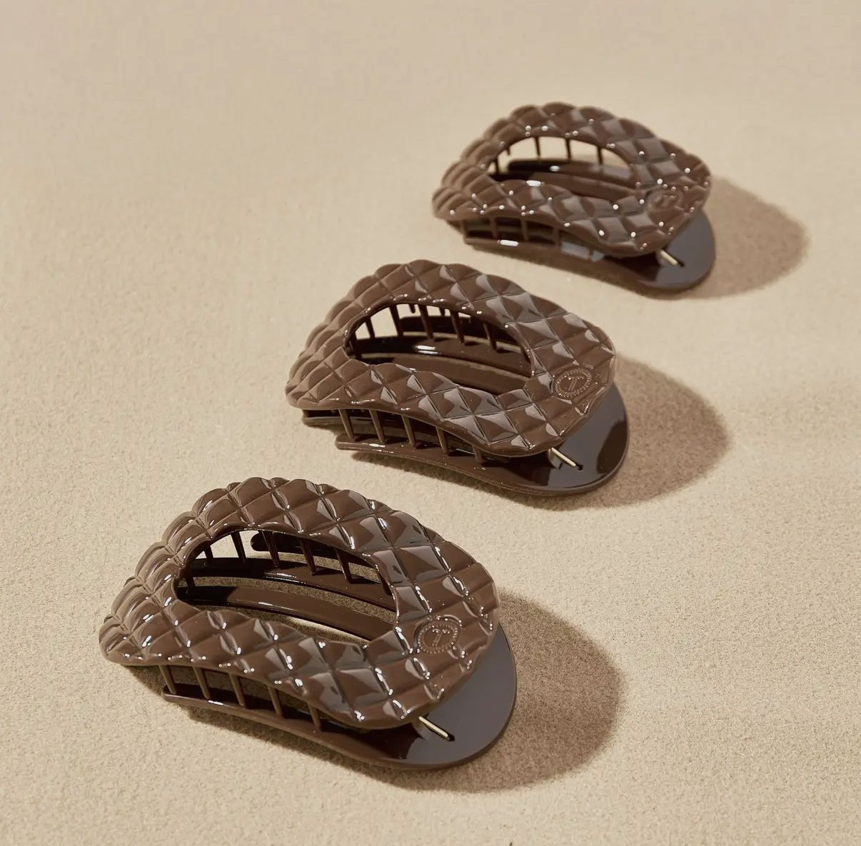 Three brown woven hair clips on a beige background