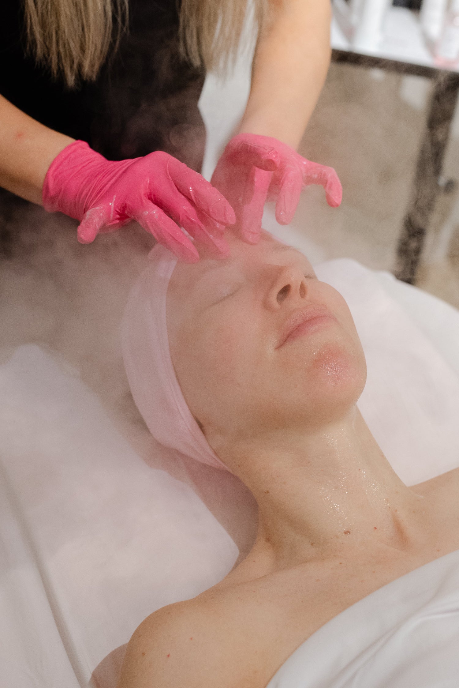 Person receiving a facial treatment with pink gloves and tools in a spa setting.