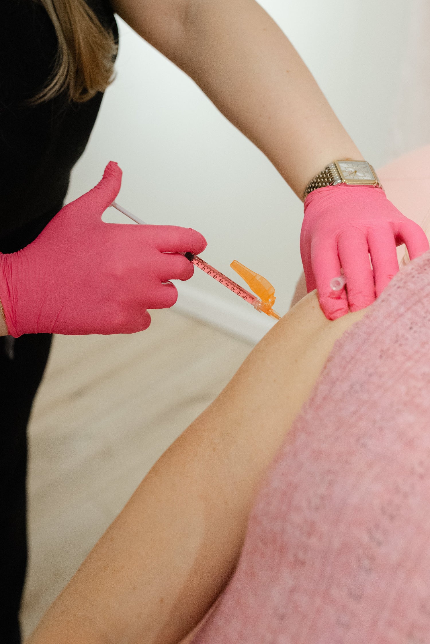 Person receiving an injection from a healthcare professional wearing pink gloves.