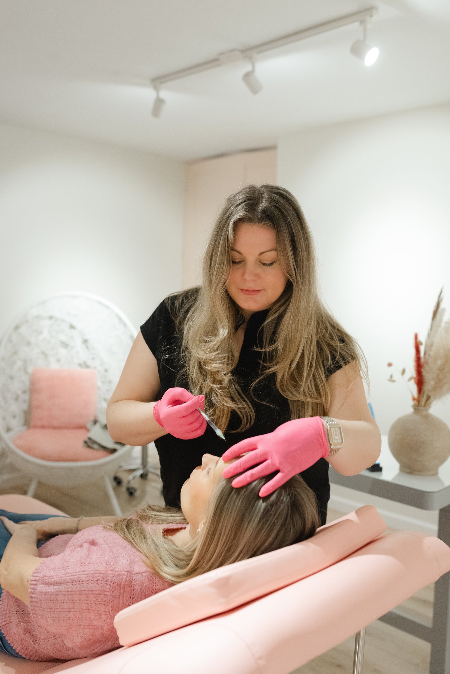 Woman getting treatment in a salon with pink gloves and chair.
